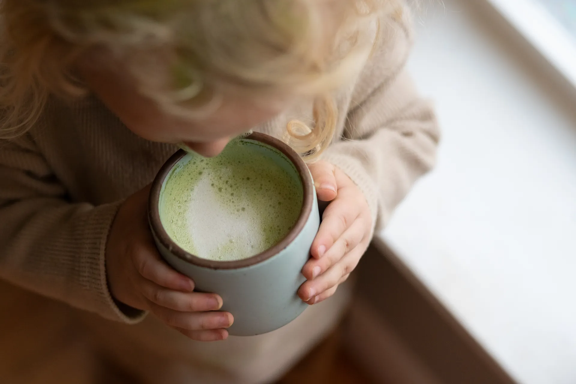 A child cradling a cup of frothy matcha