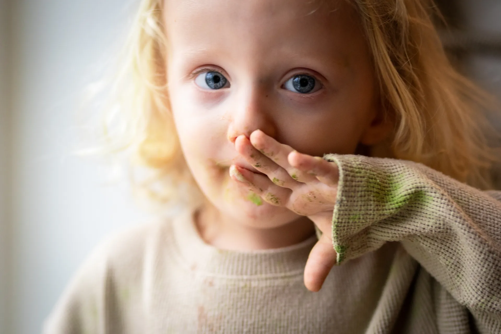 A child with matcha-dusted hands, mid-sip